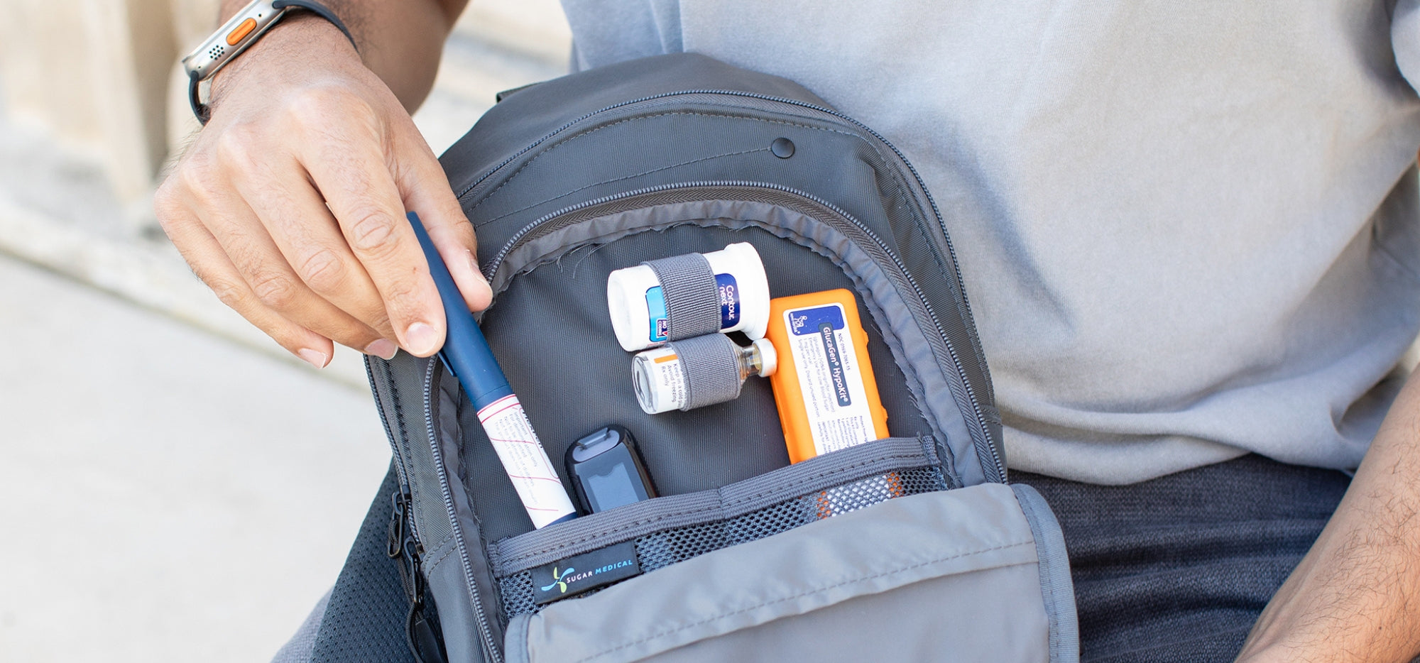 A man opening the front compartment of a Sugar Medical Diabetes Insulated Sling Backpack pulling an insulin pen out.
