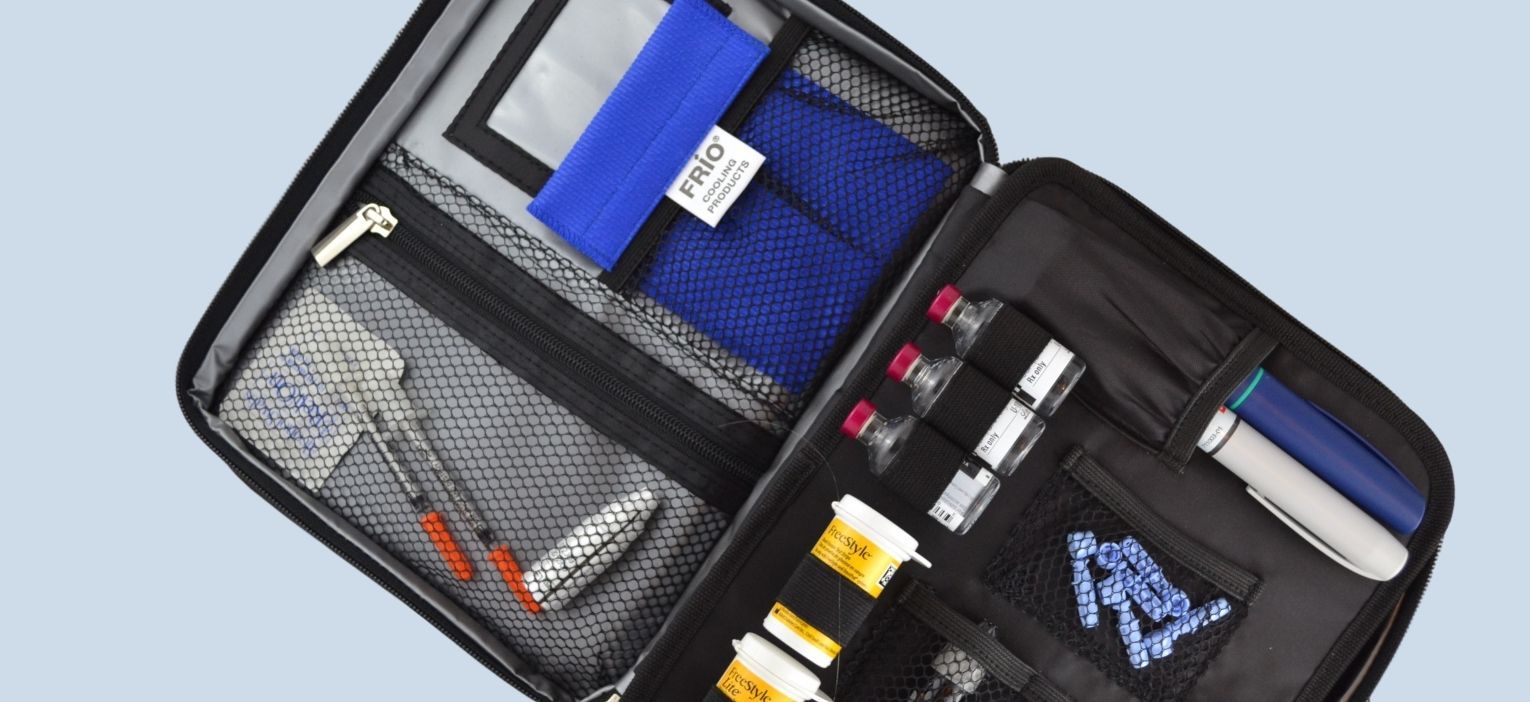 An open Diabetes Travel Bag organized with diabetic supplies on a blue RIO Insulin Cooling Case in the mesh pocket.