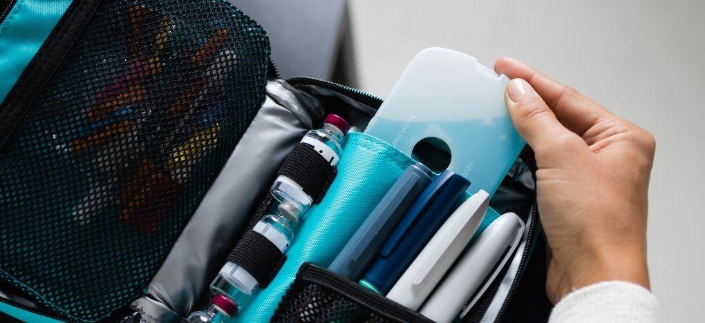 A hand pulling out an ice pack out of the insulated pocket of an Insulated Diabetes Supply Organizer that holds four insulin pens and three insulin vials securely in right side of case.