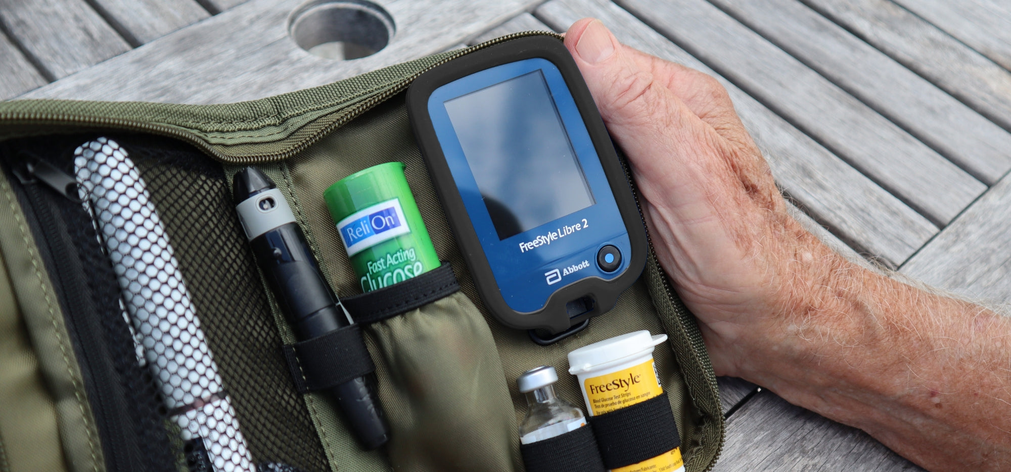 A man holding open a green diabetes supply case with a black Silicone Gel Protective Cover on his Freestyle Libre.