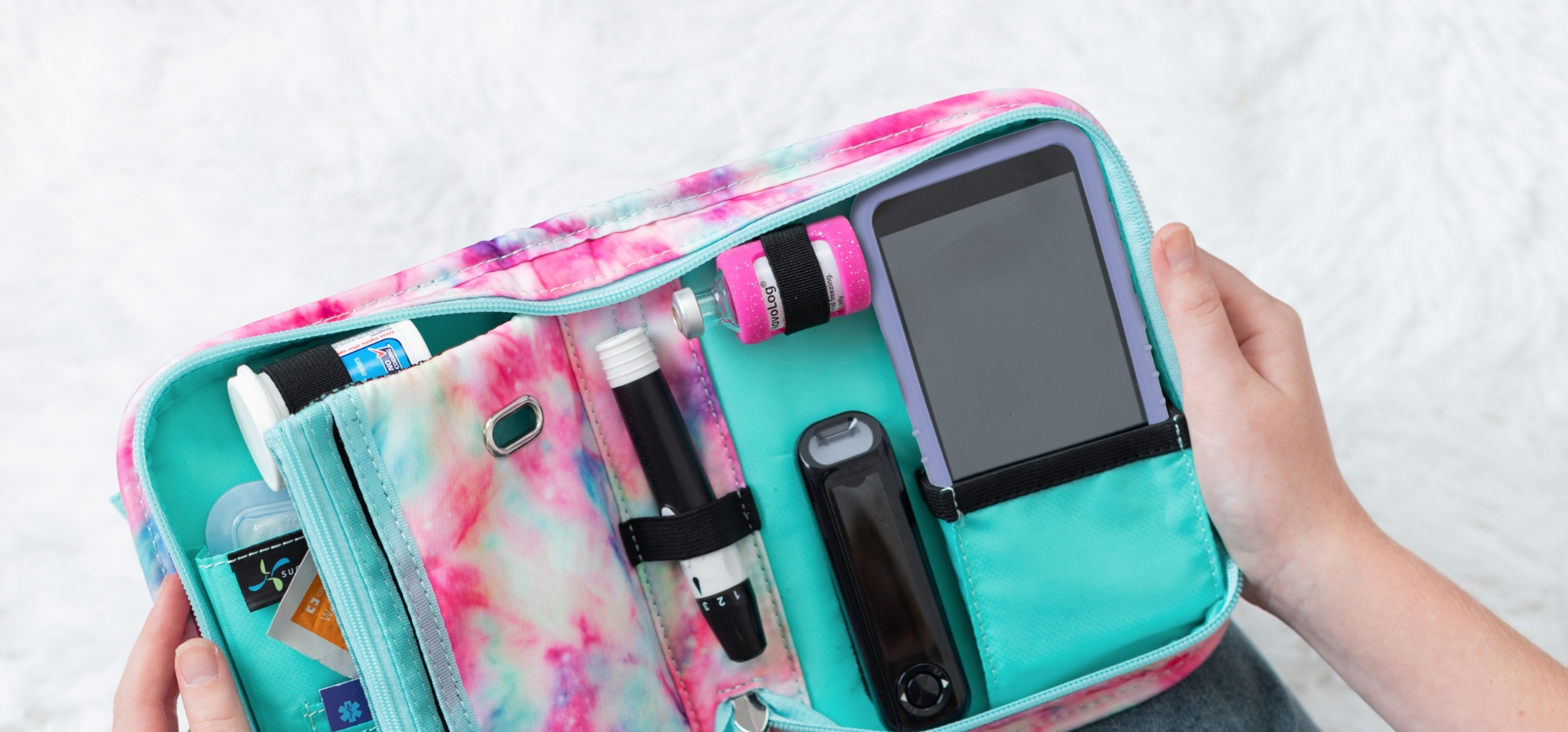 A girl holding a Omnipod Diabetes Supply Case in pink and aqua opened organized with an Omnipod 5 device secured in pocket in the case.