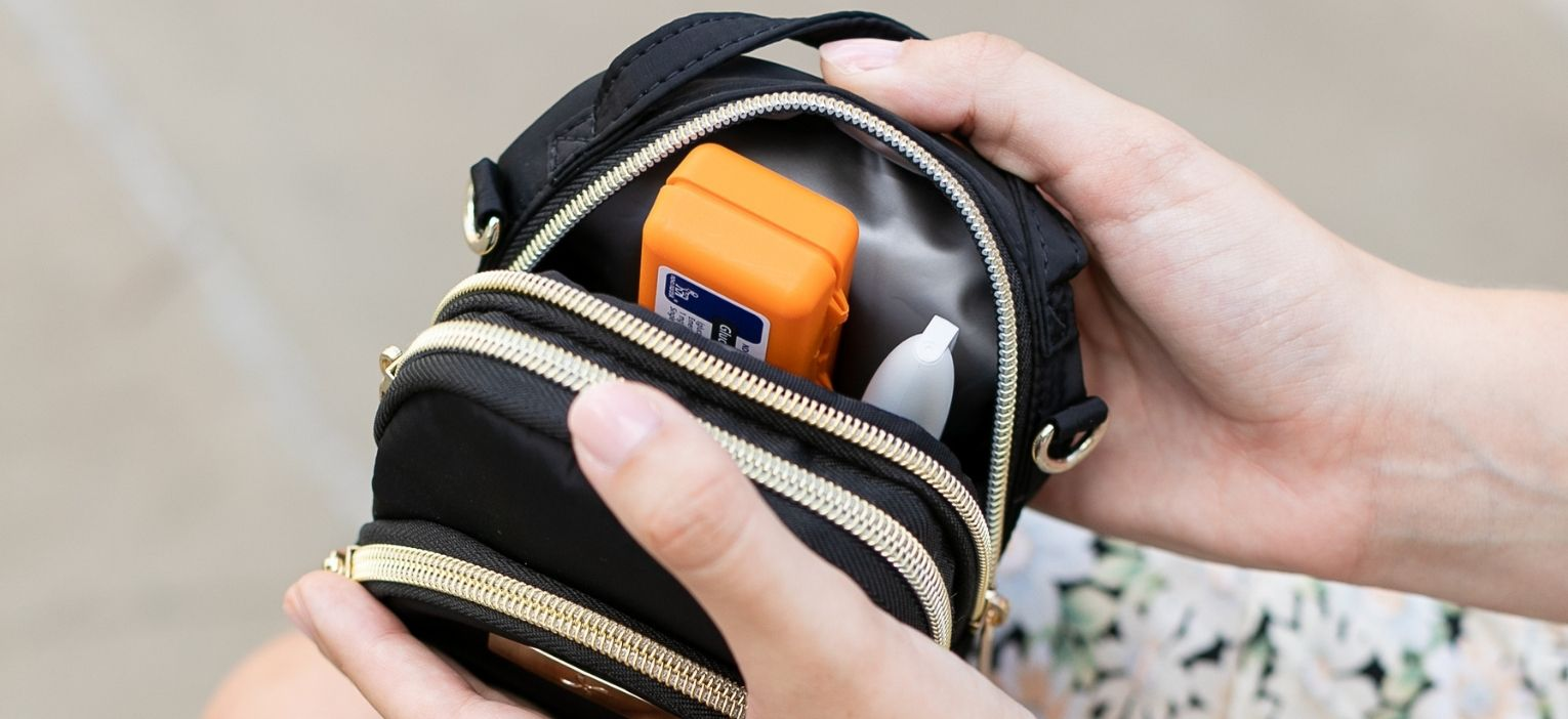 Women holding black Triple Zip Diabetes Purse open the back insulated pocket open with a glucagon, insulin open and ice pack in it.