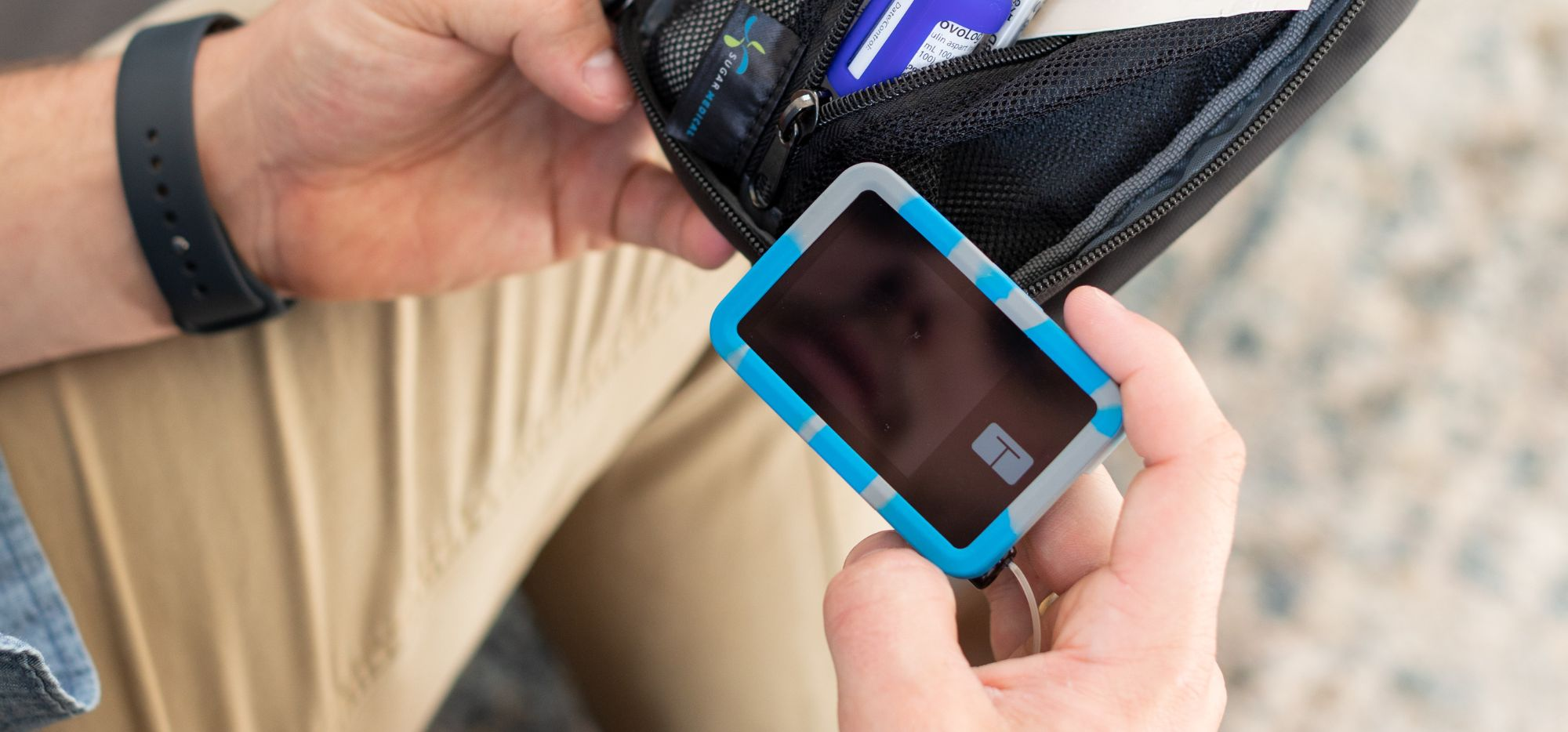 A man holding a t:slim Tandem insulin pump with a blue and grey Tandem Silicone Gel Protective Cover on it for protection.