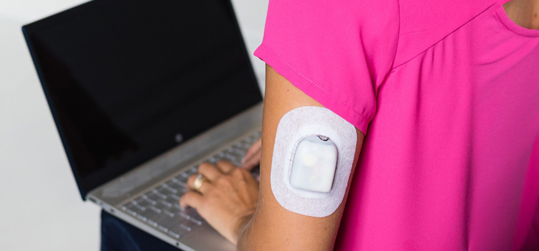 Woman in pink top working on computer with a Omnipod Pod on her arm secured with a  Podpal.
