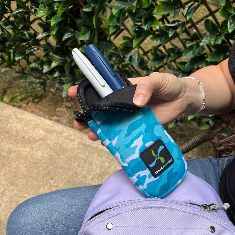 Women holding blue camo neoprene insulin pen pouch with two insulin pens and an insulin vial with an aqua Sugar Medical protective sleeve on it.