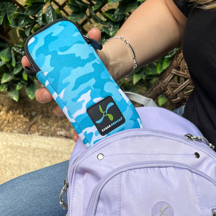 Women pulling out blue camo neoprene insulin pouch from a Sugar Medical light purple sling backpack.