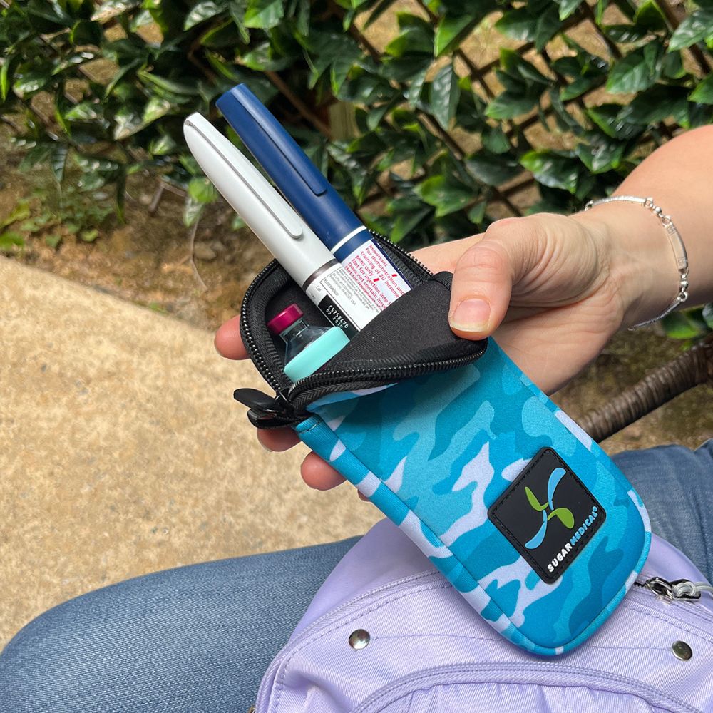 Women holding blue camo neoprene insulin pen pouch with two insulin pens and an insulin vial with an aqua Sugar Medical protective sleeve on it.