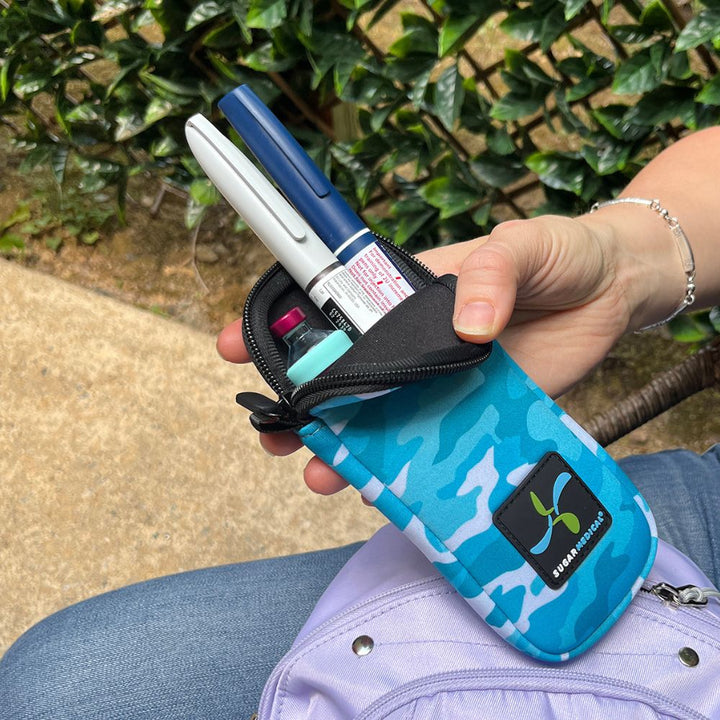 Women holding blue camo neoprene insulin pen pouch with two insulin pens and an insulin vial with an aqua Sugar Medical protective sleeve on it.