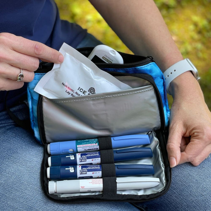 A women sitting with the blue wave Insulated Diabetes Insulin Supply Case open on her lap pulling the ice pack out of insulted pocket showing four insulin pens secured in loops.