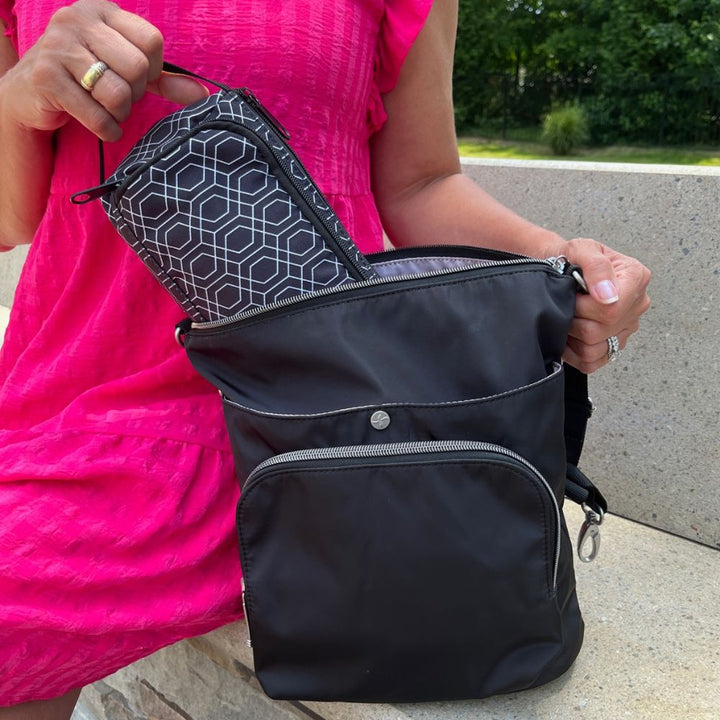 A women sitting pulling the black and white geometric pattern Insulated Diabetes Insulin Supply Case out of a black backpack by handle.