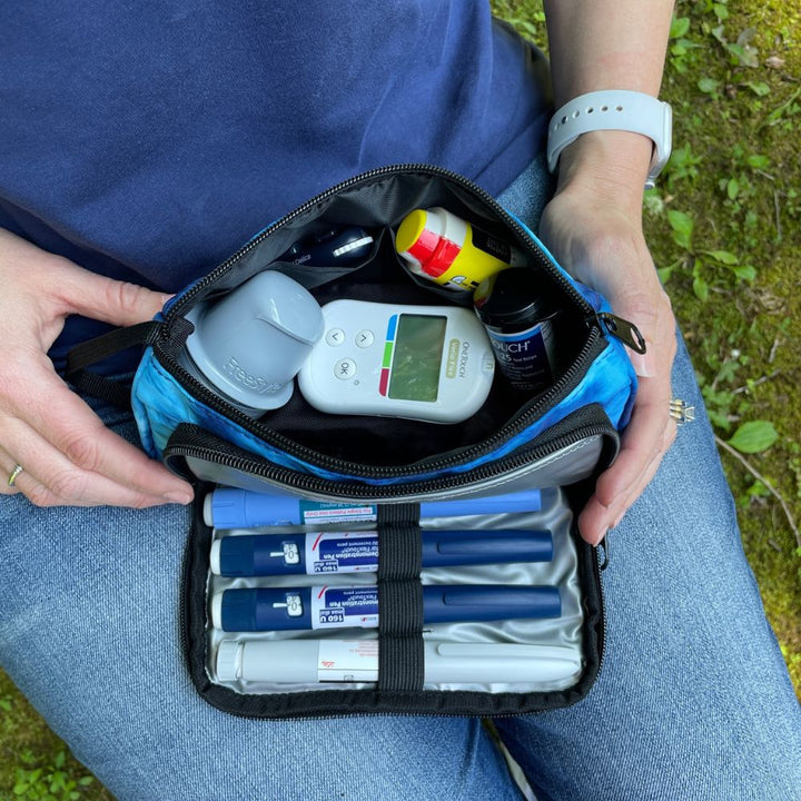 A women sitting with the blue wave Insulated Diabetes Insulin Supply Case back compartment open with diabetic supplies in it on her lap.