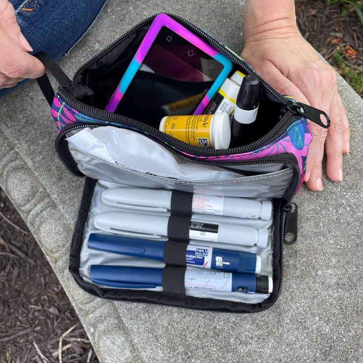 A women sitting with the blue floral pattern Insulated Diabetes Insulin Supply Case back compartment open with diabetic supplies in it on her lap.