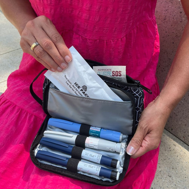 A women sitting with the black and white geometric pattern Insulated Diabetes Insulin Supply Case open on her lap pulling the ice pack out of insulted pocket showing four insulin pens secured in loops.