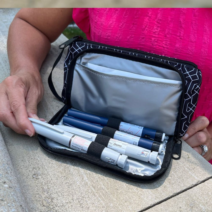 A women sitting with the black and white geometric pattern Insulated Diabetes Insulin Supply Case open on her lap pulling an insulin pen out of secured loop.