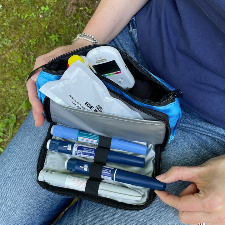 A women sitting with the blue wave Insulated Diabetes Insulin Supply Case open on her lap pulling a insulin pen out of secured loop.