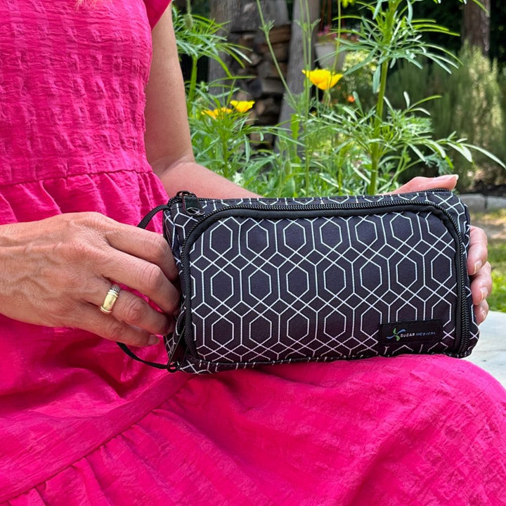 A women sitting with the black and white geometric pattern Insulated Diabetes Insulin Supply Case on her lap holding the side handle.