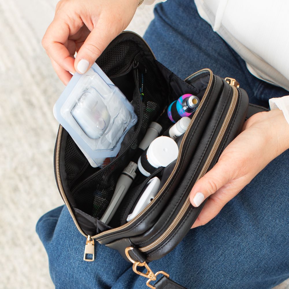Omnipod supplies neatly organized inside the Black Essential Diabetes Purse, with a hand pulling out a single pod from a designated compartment.