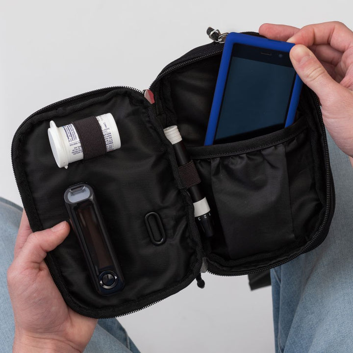 Diabetes Insulated Convertible Belt Bag in Black opened on man's lap with diabetic supplies in it and a man's hand pulling Omnipod Dash out.