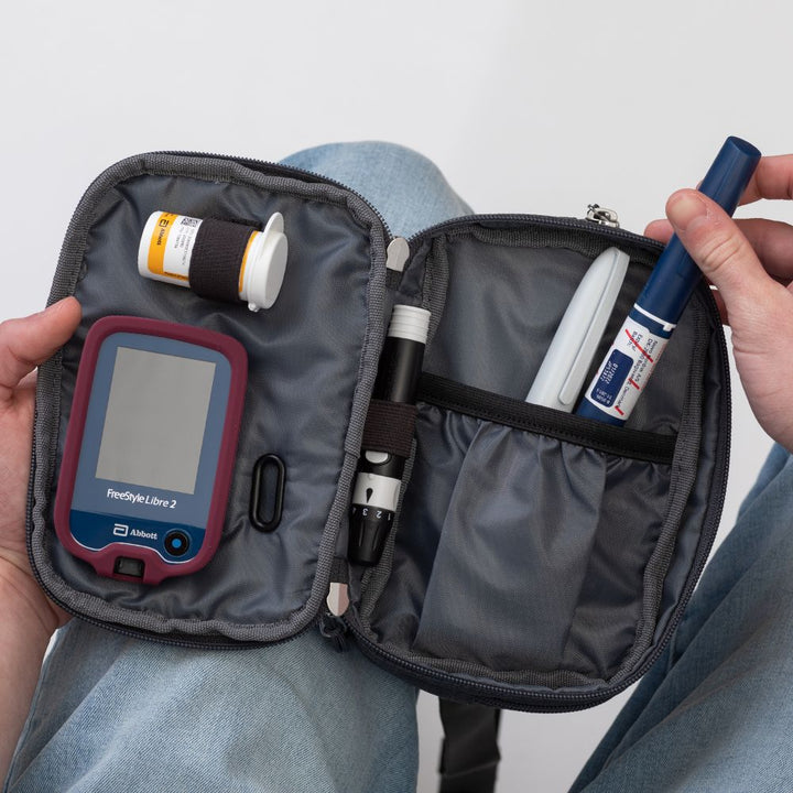 Diabetes Insulated Convertible Belt Bag in Grey opened on man's lap with diabetic supplies in it with man pulling out a insulin pen.