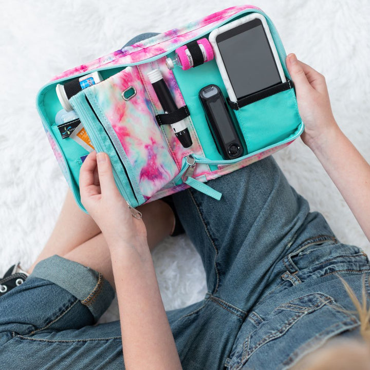 A girl opening the Dream pink and purple Omnipod supply case on her lap showing all the diabetic supplies organizer.