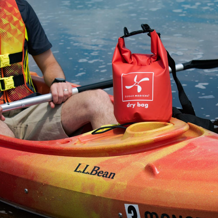 Sugar Medical red dry bag sitting on a kayak with a man in the kayak on water.