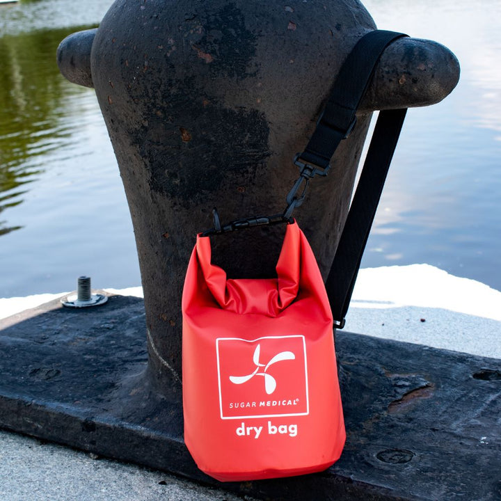Sugar Medical red dry bag hooked with shoulder strap hooked on a nig medal structure in front of the river.