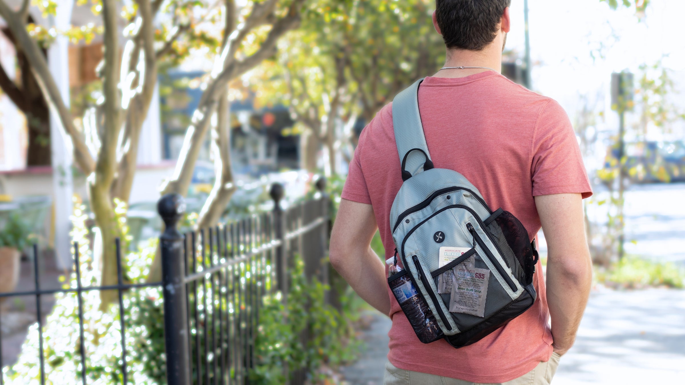 Sugar Medical Insulated Diabetes Sling Backpack in light grey on man's back with glucose SOS in the front mesh pocket. 