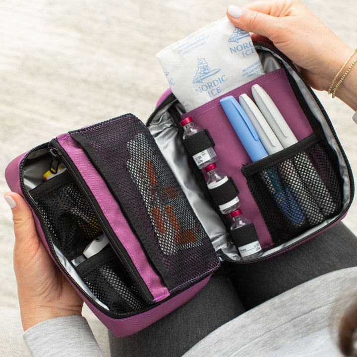Women pulling out an ice pack in the Orchid Insulated Organizer open on her lap with diabetes supplies organized in it.
