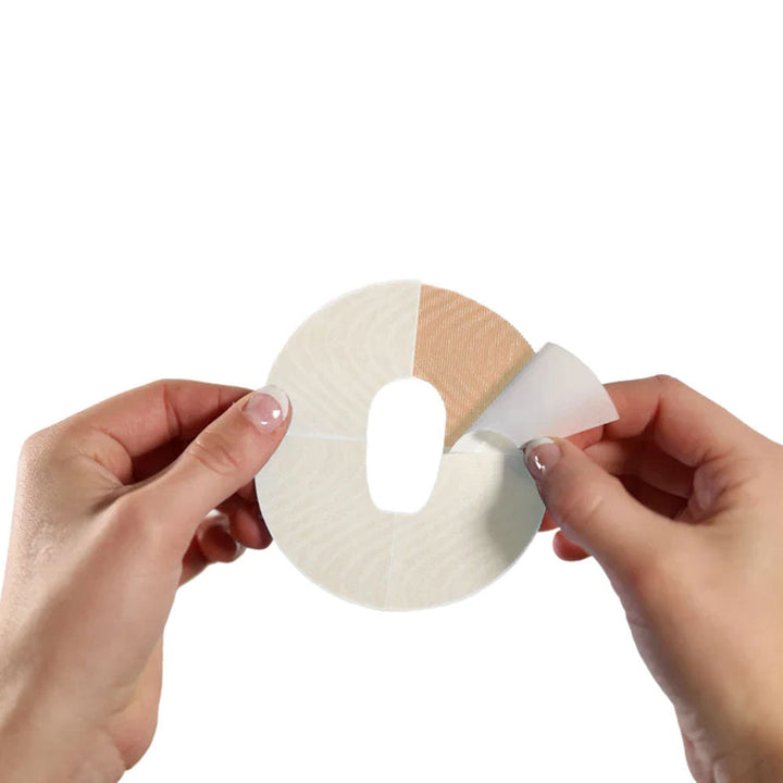 Two hands holding the tan/light brown adhesive patch and peeling off the backing paper on one of the 4 sections