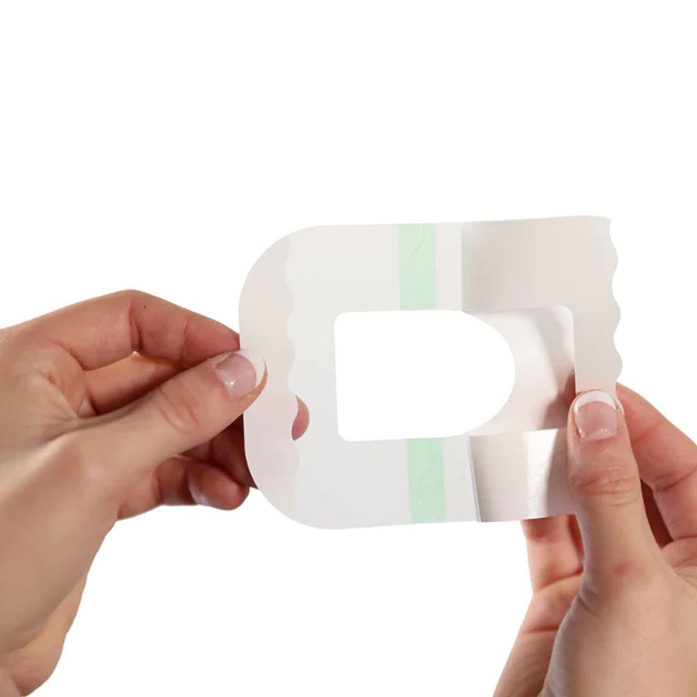 Two hands holding the omnipod clear adhesive patch and peeling off the backing paper on one of the 4 sections