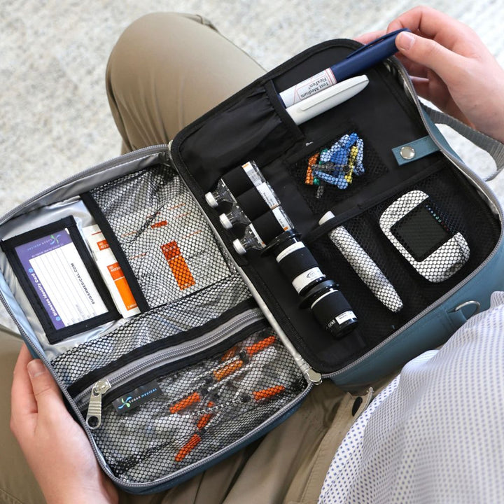 Diabetes Insulated Travel Bag in steel blue front compartment for a insulin pens, insulin vials, glucose meter and other diabetes supplies on man’s lap.