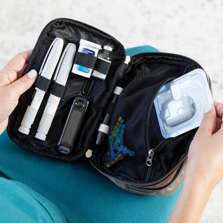 Diabetes Nylon Belt Bag inside set up with two insulin pens, glucose meter, test strips, insulin vial and mesh pocket to fit more diabetic supplies opened on a women’s lap.