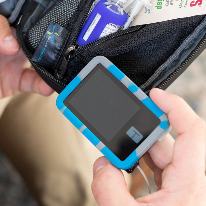 Blue and grey Tandem t:slim Gel Skin held in man’s hand showing access to see insulin pump screen.