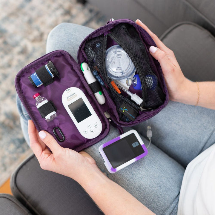 Tandem Supply Case in deep purple opened in the woman’s lap with an inside set up containing diabetic supplies while reading her tandem pump