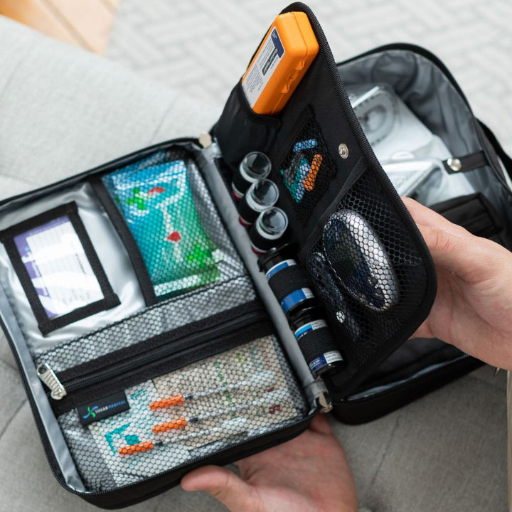 Diabetes Insulated Travel Bag in black back compartment for a glucagon kit, Tandem supplies, Dexcom, snacks, glucose tablets, and includes a removable pouch on man’s lap.