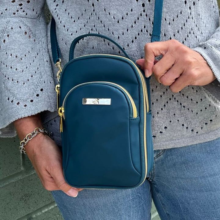 Woman wearing grey sweater and teal Meredith purse crossbody while outside. 