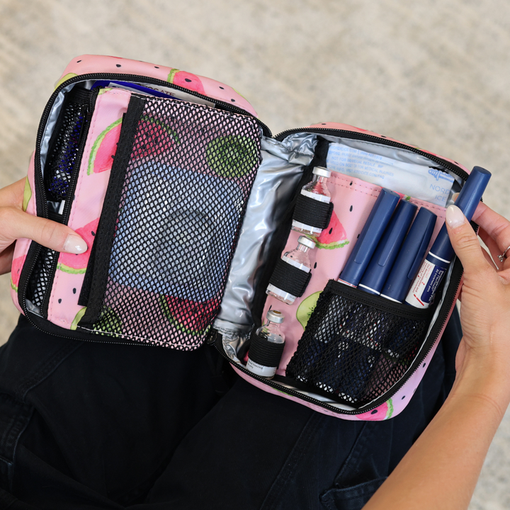 Women pulling out an insulin pen in the Watermelon Insulated Organizer open on her lap with diabetes supplies organized in it.