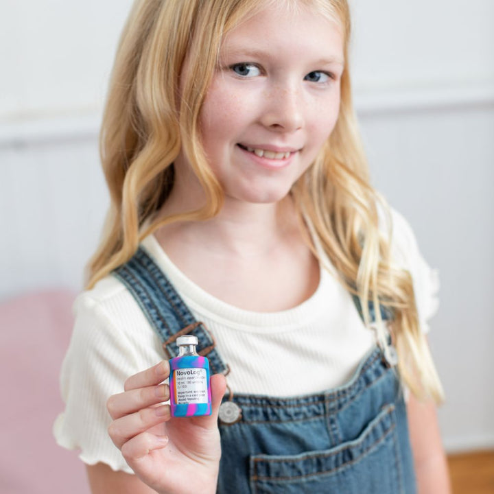 A girl holding a Novolog insulin vial with a pink and blue tie dye Insulin Vial Protective Silicone Sleeve.