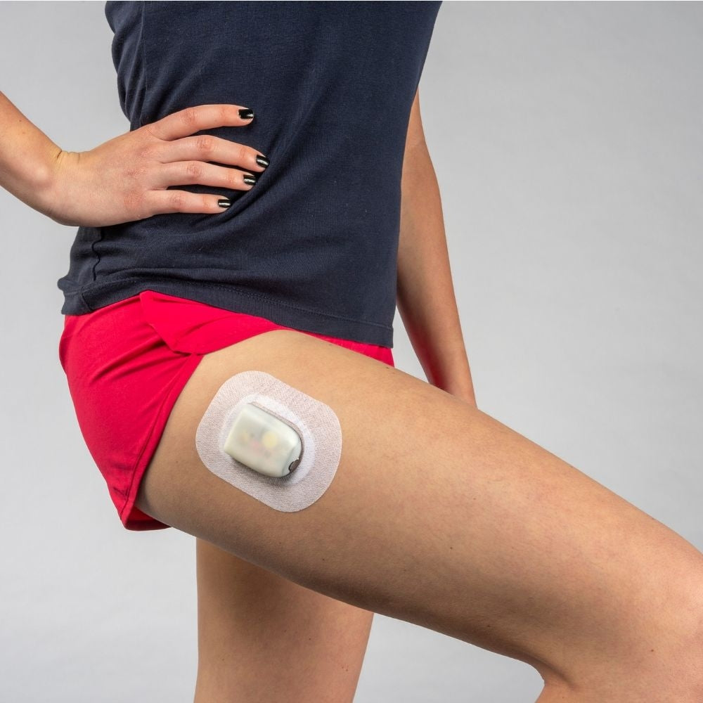 A woman in red shorts and a black shirt wearing the pod and Podpal on the right side of her upper right thigh.