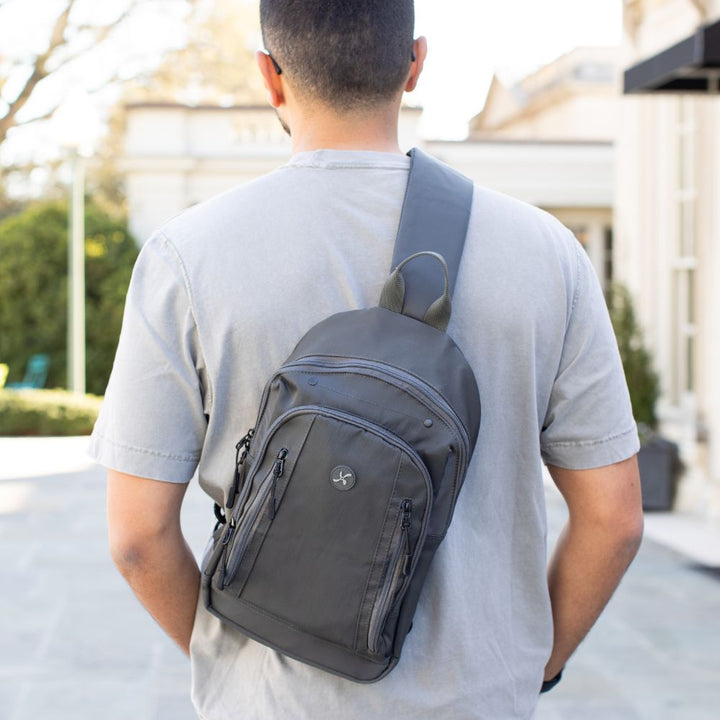 Man in grey t-shirt wearing the charcoal grey Insulated Roam Sling Backpack on his back with hand in his pocket. 