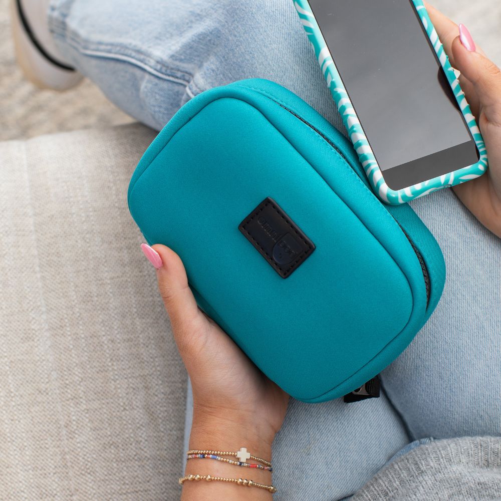Teal travel case held by a hand with a Omnipod 5on top, sitting on a gray surface.