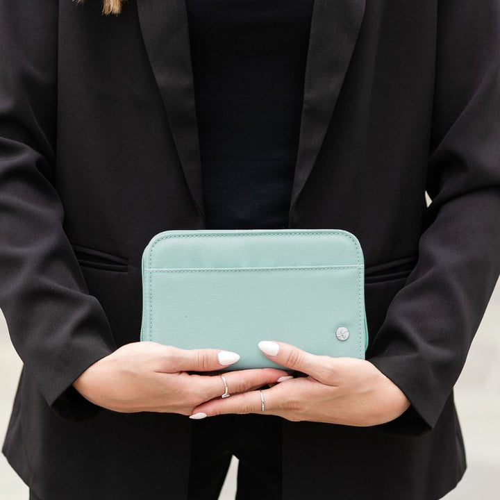 A person in a black blazer holding a seafoam diabetes supply case. The person has white manicured nails and is wearing simple silver rings.
