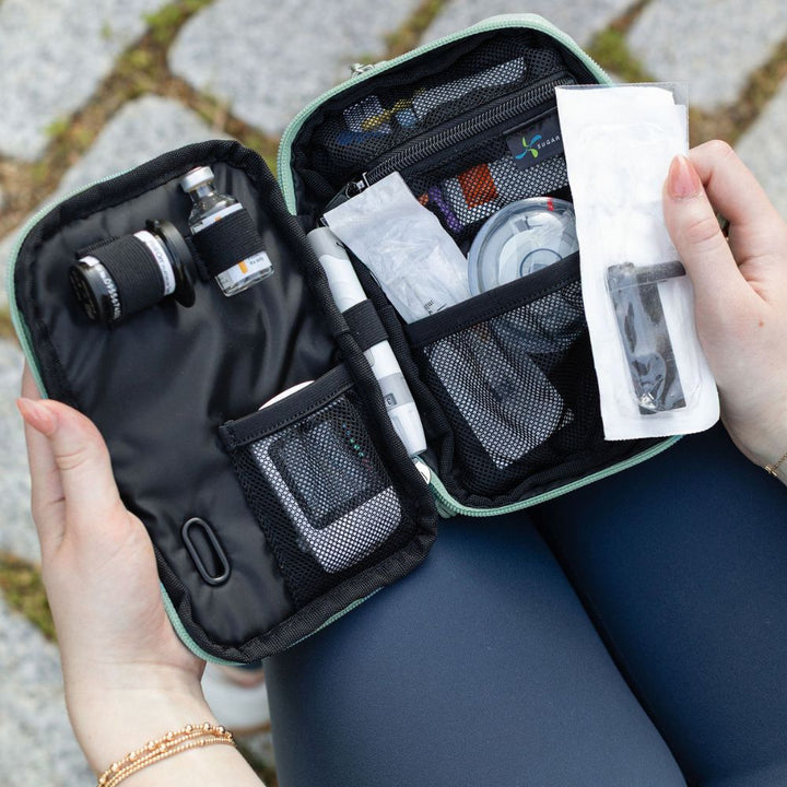 Person holding a seafoam tandem case open with diabetes supplies on a stone surface