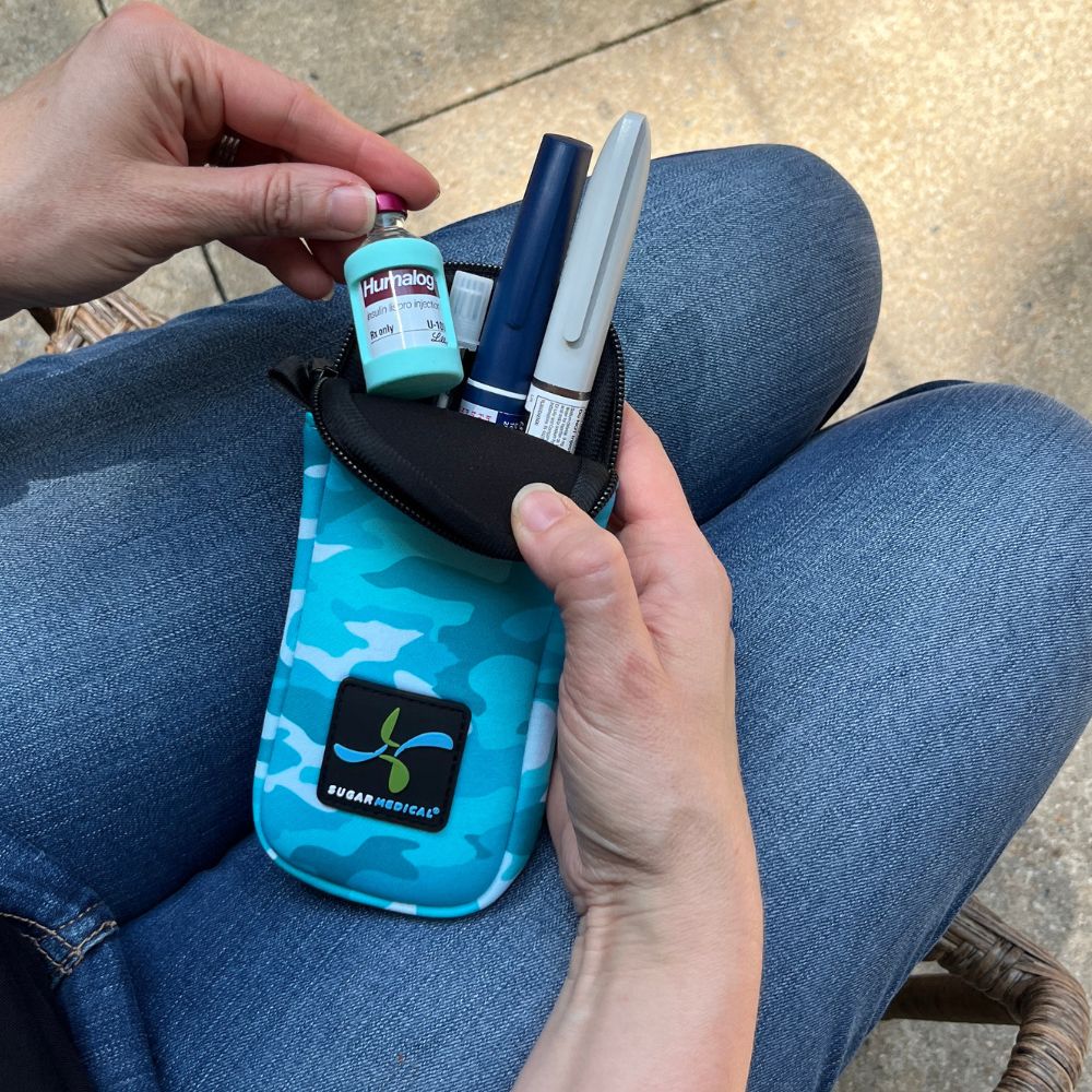 Women holding blue camo neoprene insulin pen pouch with two insulin pens and pulling out a Humalog insulin vial with an aqua Sugar Medical silicone protective sleeve. 