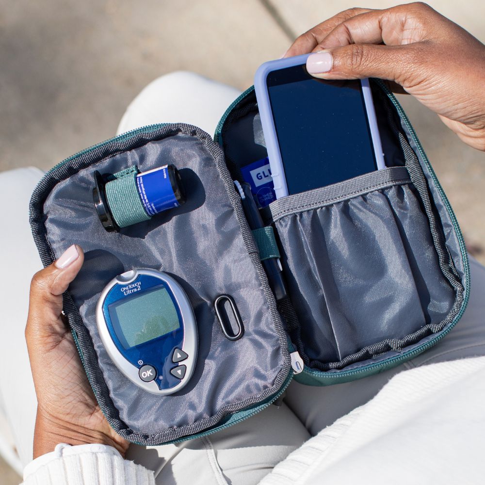 The Green Pine Diabetes Insulated Convertible Supply Bag open on a women lab with Omnipod supplies organized in the pockets and women pulling out the Omnipod 5 out.