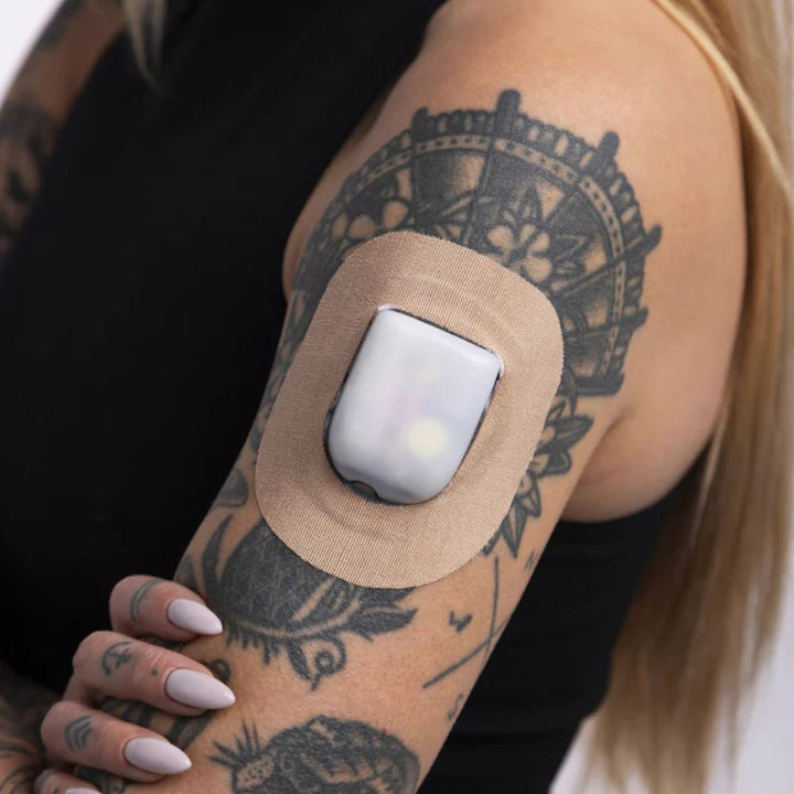 A woman in a black tank top wearing a Skin Grip tan Omnipod adhesive patch around the pod on the outside of her upper right arm