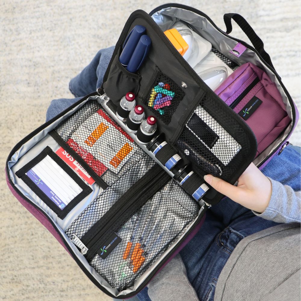 Diabetes Insulated Travel Bag in purple back compartment for a glucagon kit, Tandem supplies, Dexcom, snacks, glucose tablets, and includes a removable pouch on woman’s lap. 