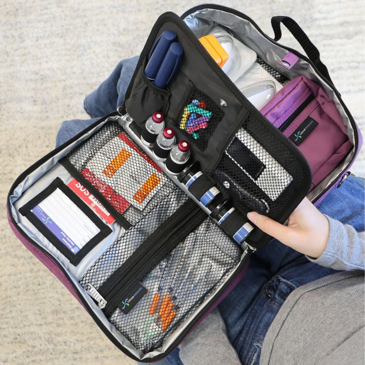 Diabetes Insulated Travel Bag in purple back compartment for a glucagon kit, Tandem supplies, Dexcom, snacks, glucose tablets, and includes a removable pouch on woman’s lap. 