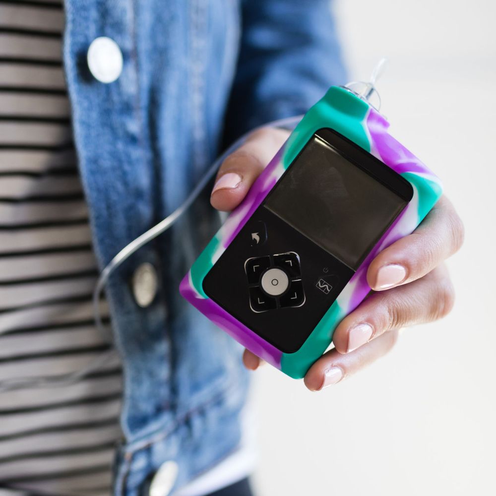 Women holding Purple, Green and White Tie-Dye Medtronic Insulin Pump Gel Skin with Medtronic Insulin pump in it. 