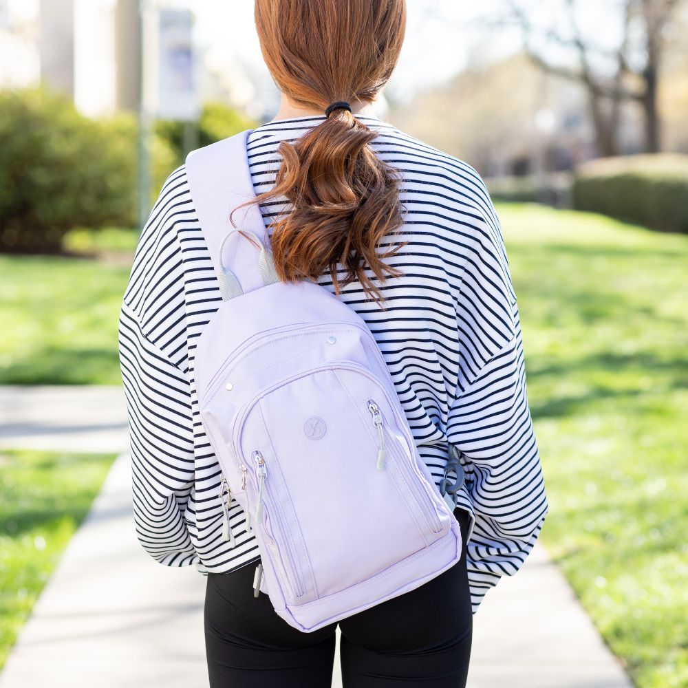 Girl with stripe top wearing the light purple Insulated Roam Sling Backpack on her back. 